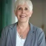 Portrait of Mary Rodwell, author and researcher, wearing a light gray blazer and smiling warmly indoors.