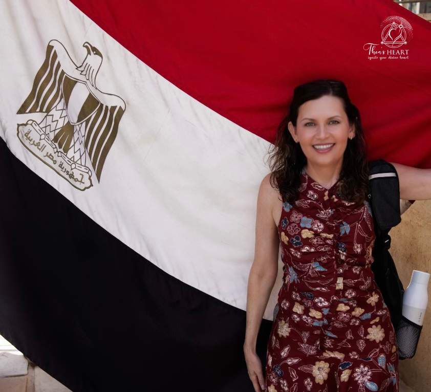 Althea Provost standing before the Egyptian flag during her Starseed Egypt Adventure 2024, smiling and carrying a backpack