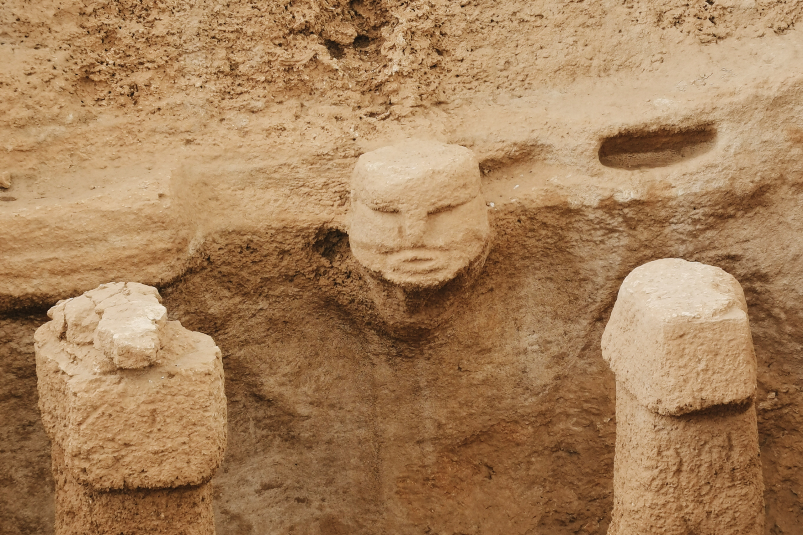 Carved stone face and upright pillars at Karahan Tepe, partially excavated within an earthen enclosure.