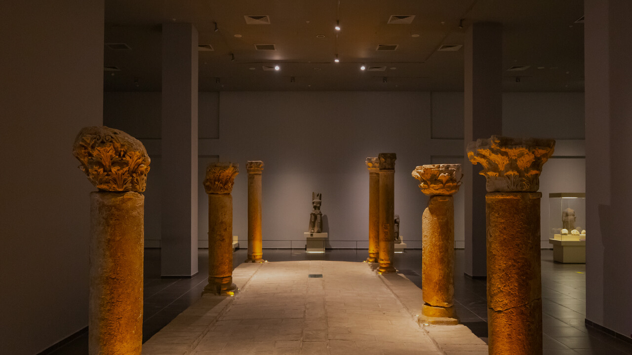 Interior view of the Şanlıurfa Archaeology Museum with illuminated ancient columns leading toward a central statue.