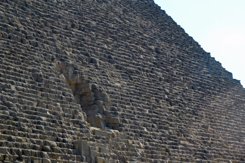 Close‑up view of the Great Pyramid’s north face showing the chevron‑shaped structure and the recessed area where the original ancient entrance lies, surrounded by large limestone blocks.