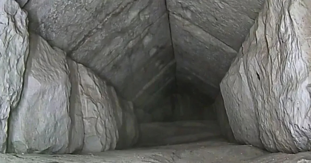 Interior of the 30‑foot corridor discovered behind the chevron‑shaped structure on the Great Pyramid’s north face, showing a narrow stone passage with corbelled limestone blocks and an unfinished floor extending into darkness
