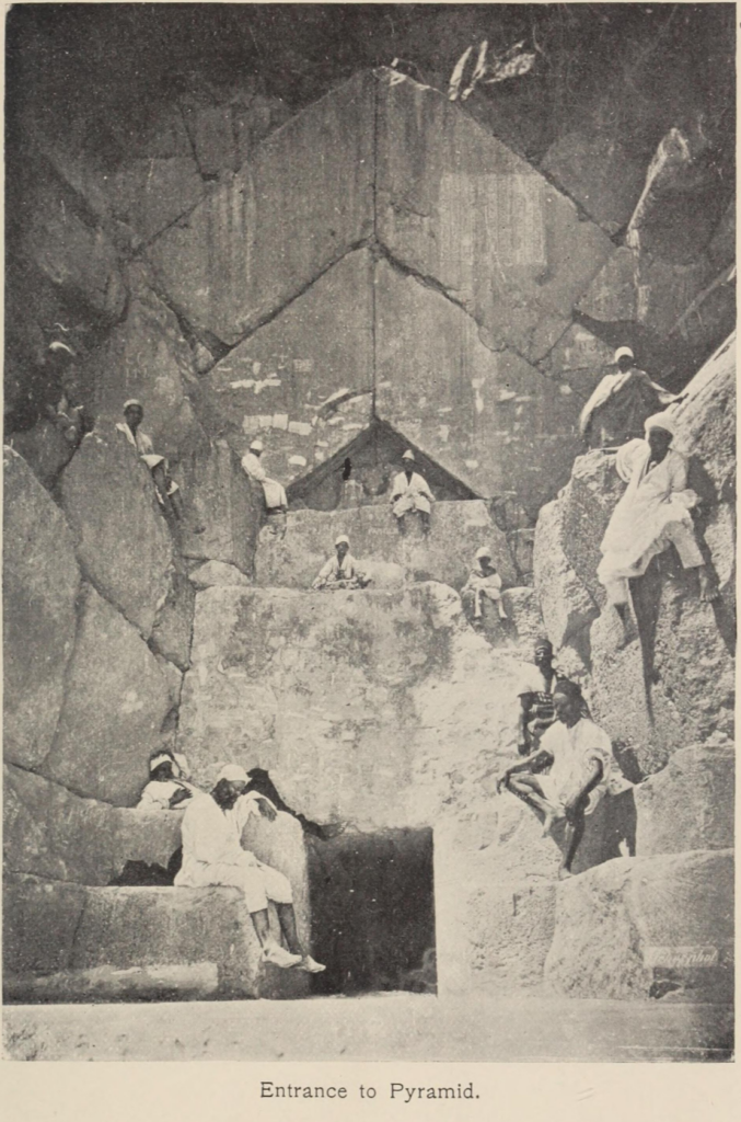 Chevron-shaped structure above the Great Pyramid entrance with visitors seated on massive limestone blocks, c. 1895