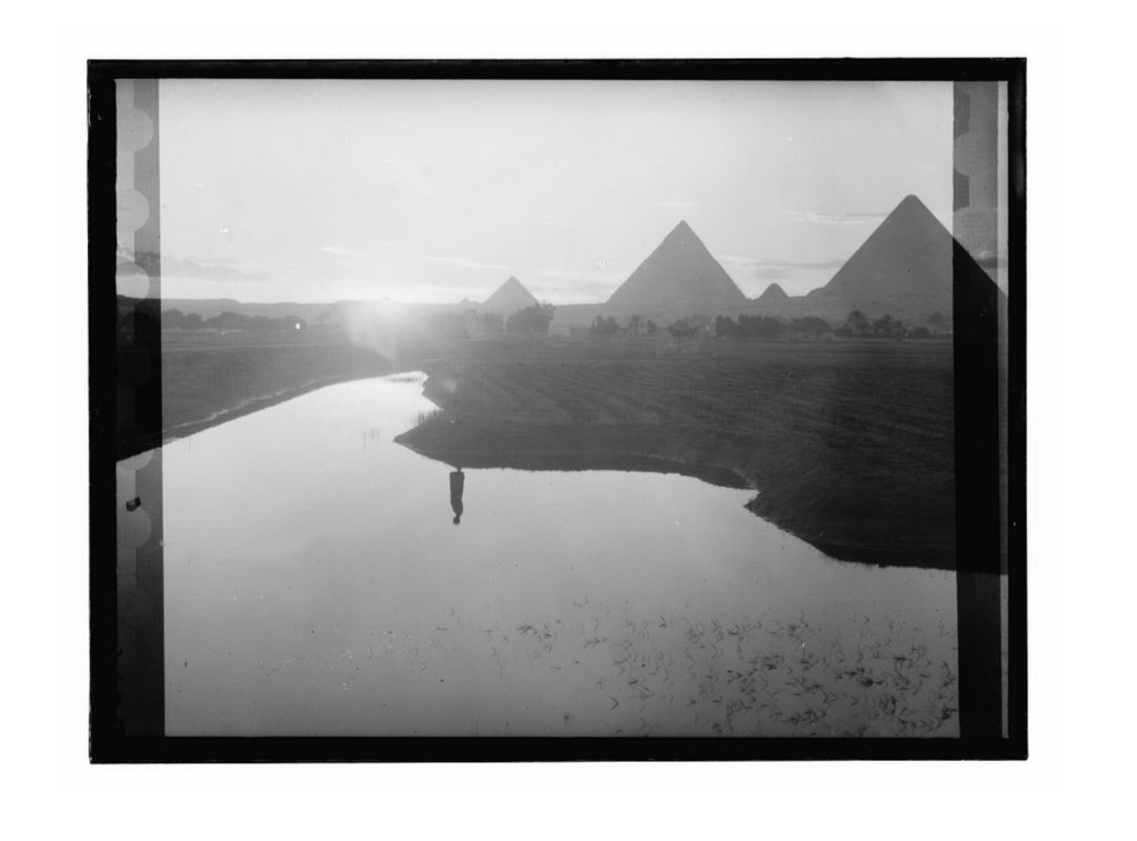 Evening view of the Nile overflow with a silhouetted figure near the water and the pyramids in the distance, 1936