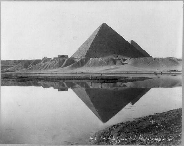 Chevron-shaped structure above the Great Pyramid entrance with two men standing on a shoal between the pyramid and its reflection during Nile flood, Bonfils No. 1435