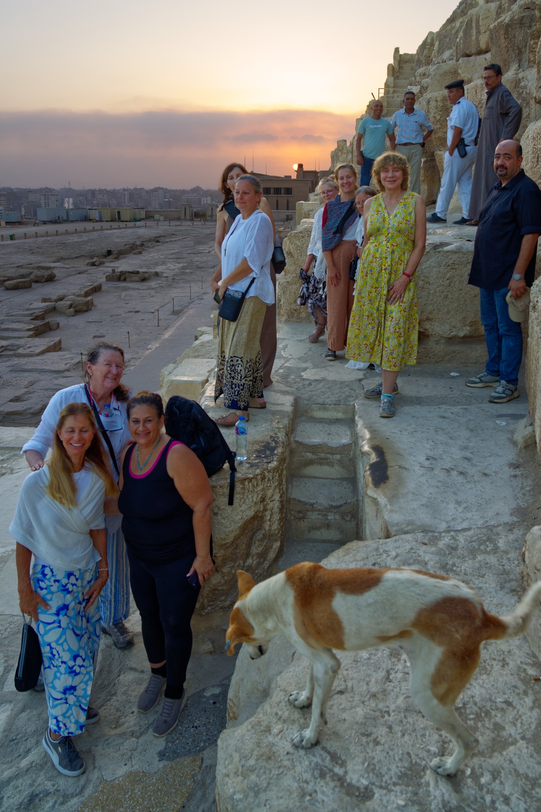 A group from the Starseed Egypt Adventure 2024 with Althea Provost stands on the stone steps of the Great Pyramid in the early morning light, with Boka the dog in the foreground after waiting by the Robber’s Entrance as they exited their private interior experience.