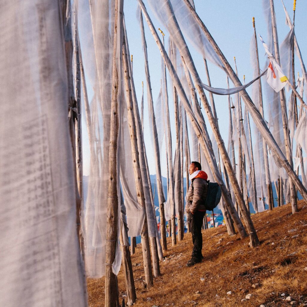 Starseed Bhutan Adventure with Althea Provost, man standing on a hillside among tall white prayer flags.