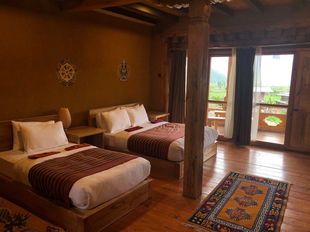 Starseed Bhutan Adventure with Althea Provost — ABC Eco Lodge room with two beds, wooden interiors, and balcony views of the surrounding hills.